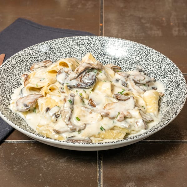 Creamy mushroom pasta in a decorative bowl, garnished with fresh herbs, on a dark tiled surface.