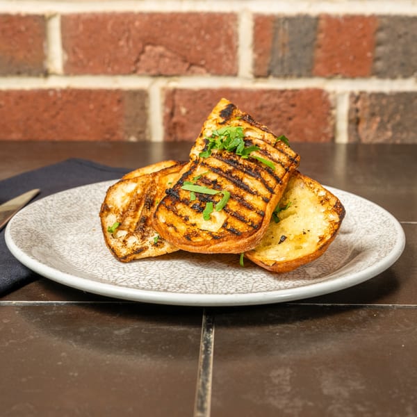 Grilled Italian bread slices, topped with fresh parsley, on a white plate with a brick background.