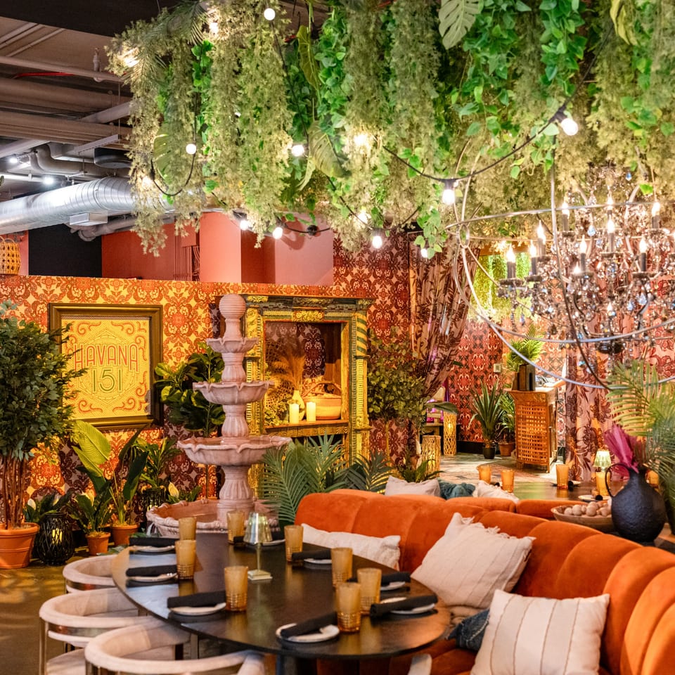 Lush, tropical-themed dining area with orange banquettes, a fountain, and hanging greenery at Lena's.