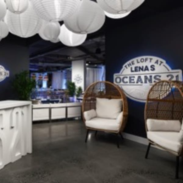 A lounge area with two wicker chairs, a white reception desk, and a Lena's Oceans 21 sign.