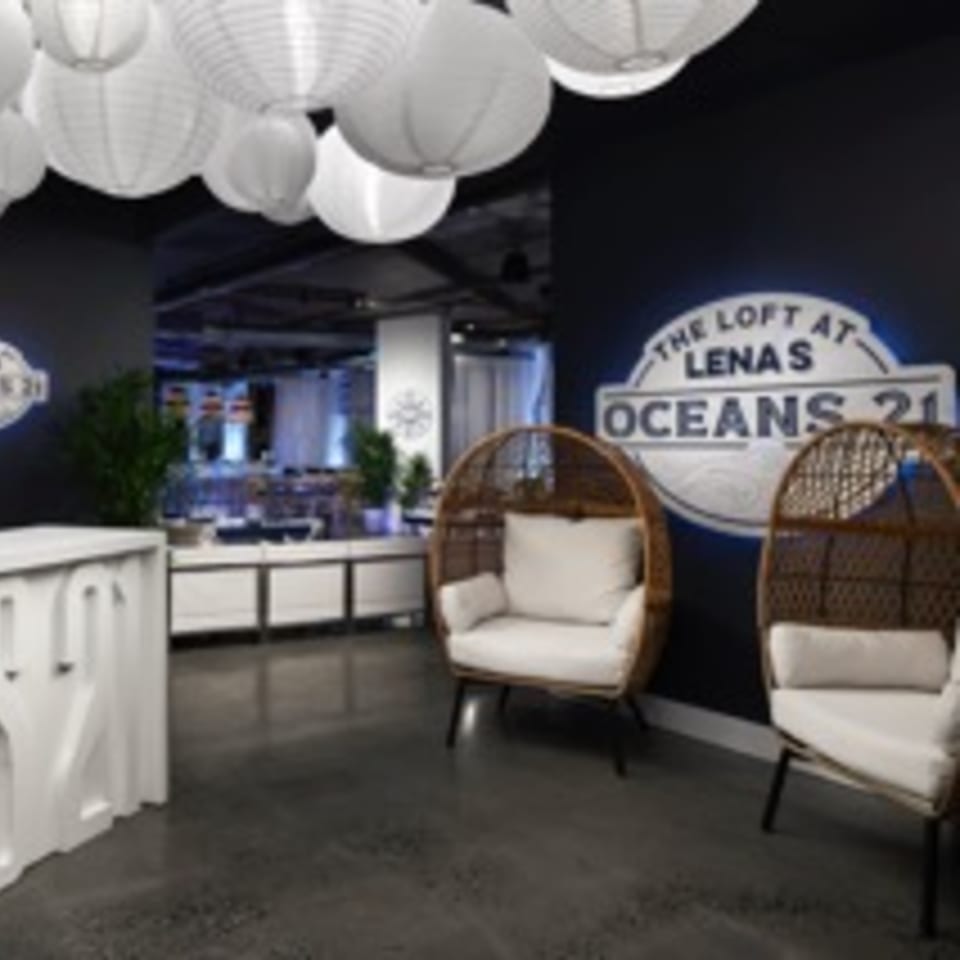 A lounge area with two wicker chairs, a white reception desk, and a Lena's Oceans 21 sign.