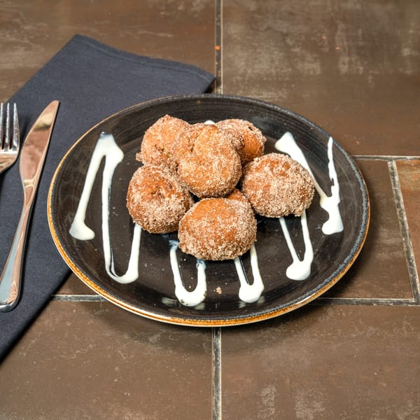 Lena's Wood-Fired Pizza & Tap's cinnamon sugar zeppole with white icing drizzle on a dark plate.