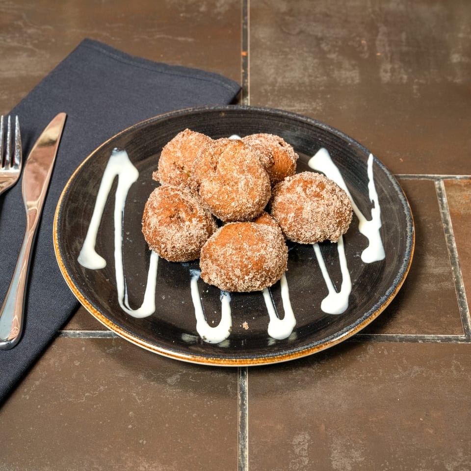 Lena's Wood-Fired Pizza & Tap's cinnamon sugar zeppole with white icing drizzle on a dark plate.