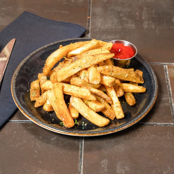 A plate of golden-brown french fries, seasoned with herbs and parmesan, with a side of ketchup.