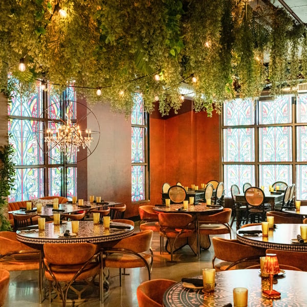 Lena's Wood-Fired Pizza & Tap dining room with hanging greenery, stained glass windows, and ornate tables.