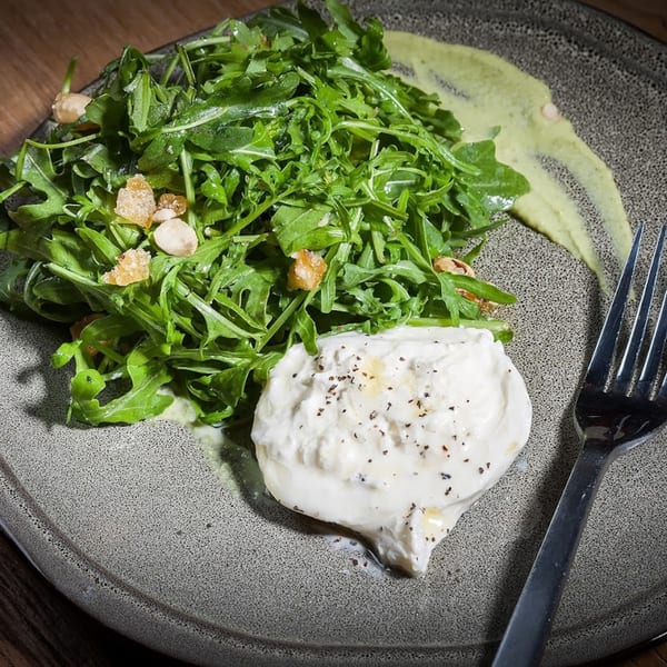 A Lena's Wood-Fired Pizza & Tap burrata dish with arugula, nuts, and a green sauce.