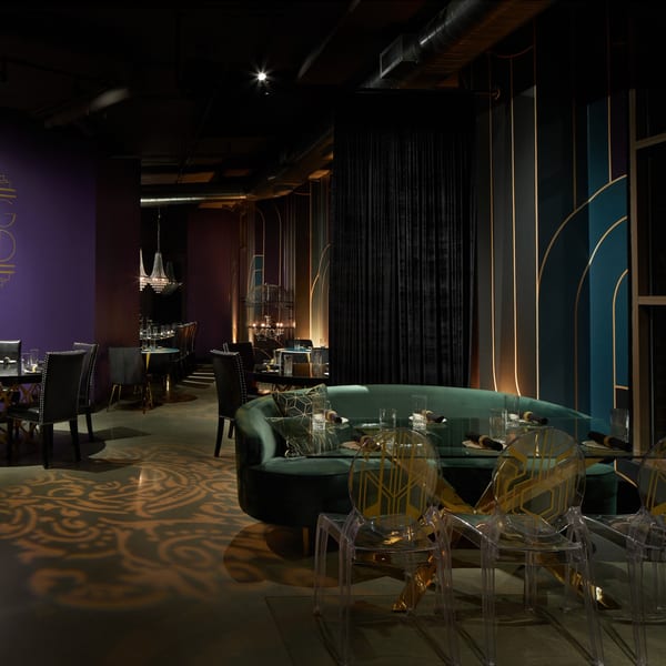 Lena's Wood-Fired Pizza & Tap's dimly lit dining room with green velvet banquettes and clear chairs.