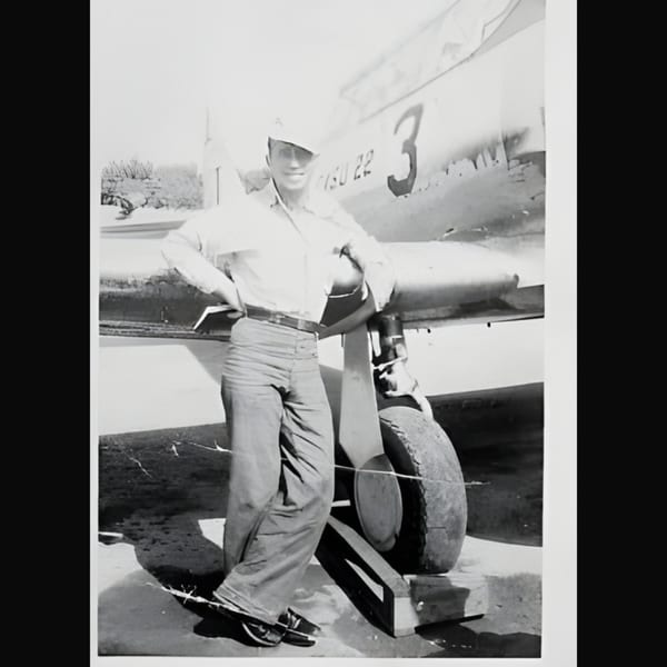 A man in a cap and light-colored clothing stands next to a small airplane.