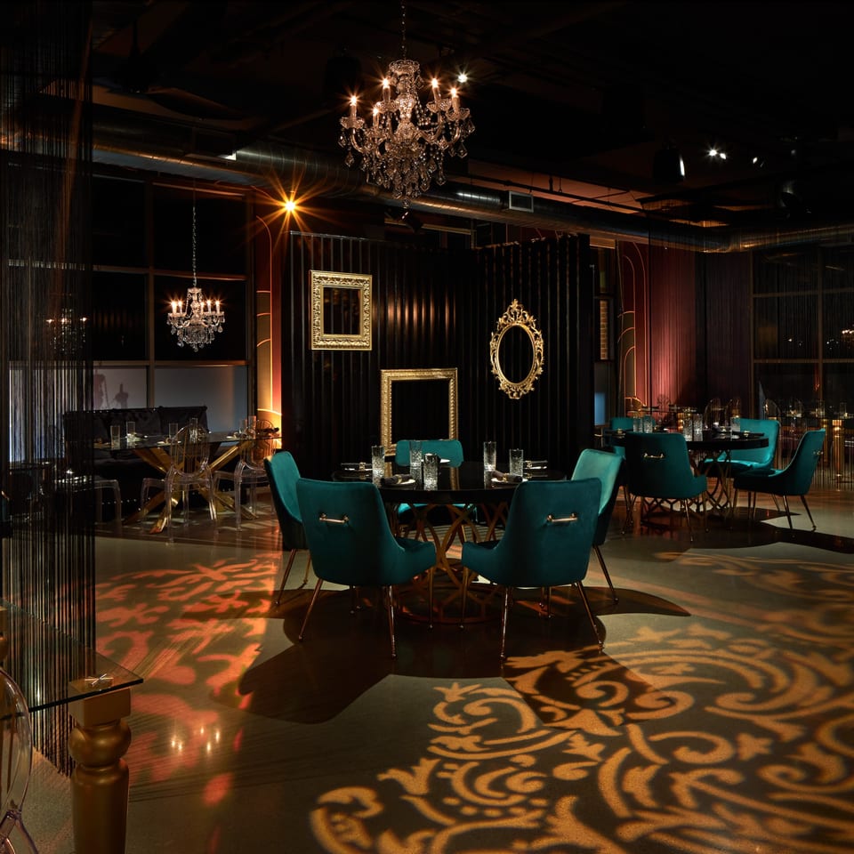 Lena's Wood-Fired Pizza & Tap dining room with teal chairs, dark tables, chandeliers, and patterned floor lighting.