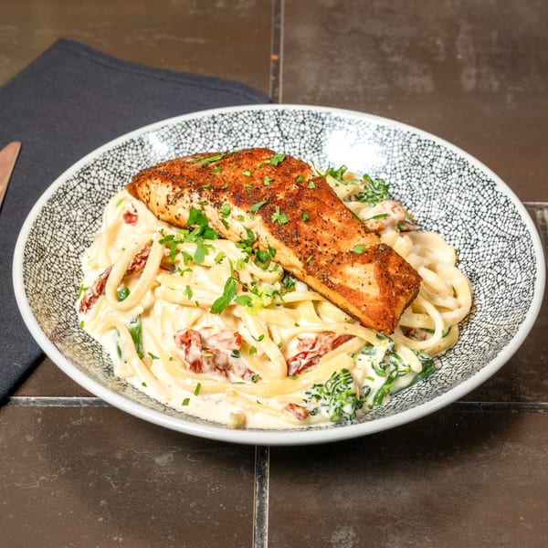 Lena's Wood-Fired Pizza & Tap's creamy pasta with sun-dried tomatoes, spinach, and a seasoned salmon fillet.