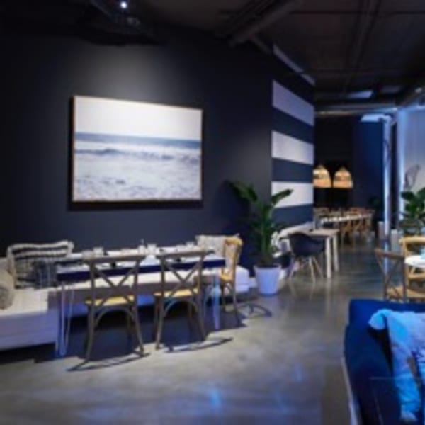 Dining area with dark blue walls, a large ocean art print, and light wood tables and chairs.