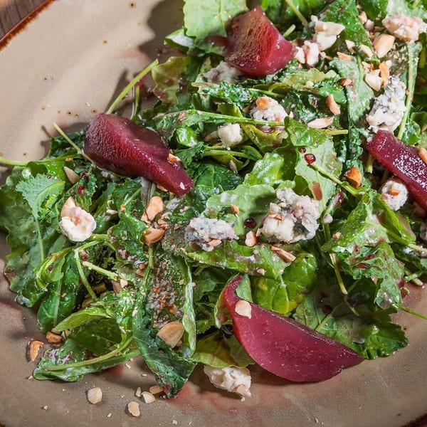 Close-up of a fresh green salad with red pear slices, crumbled cheese, and nuts.