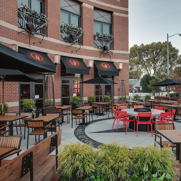 Lena's Wood-Fired Pizza & Tap's outdoor patio with tables, red chairs, umbrellas, and large spider decorations.