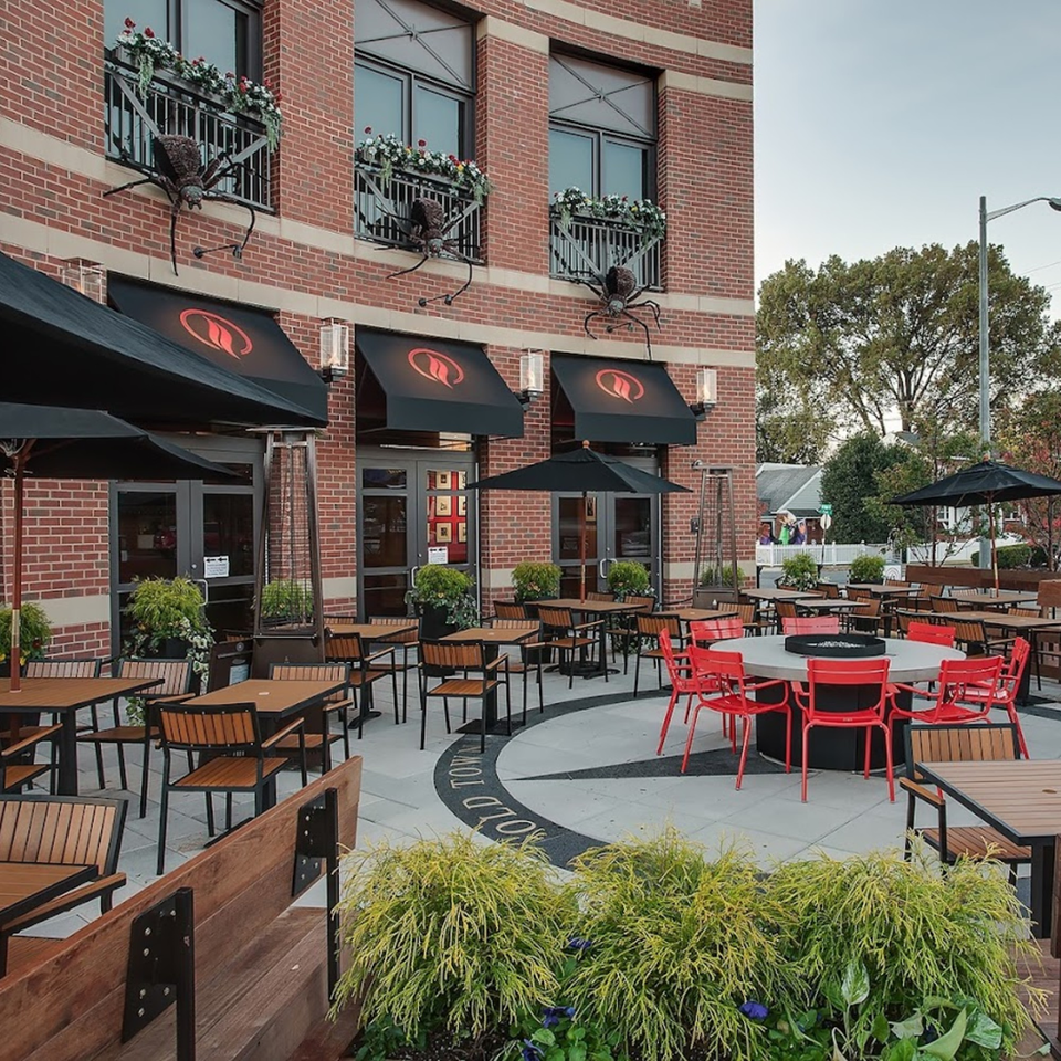Lena's Wood-Fired Pizza & Tap's outdoor patio with tables, red chairs, umbrellas, and large spider decorations.