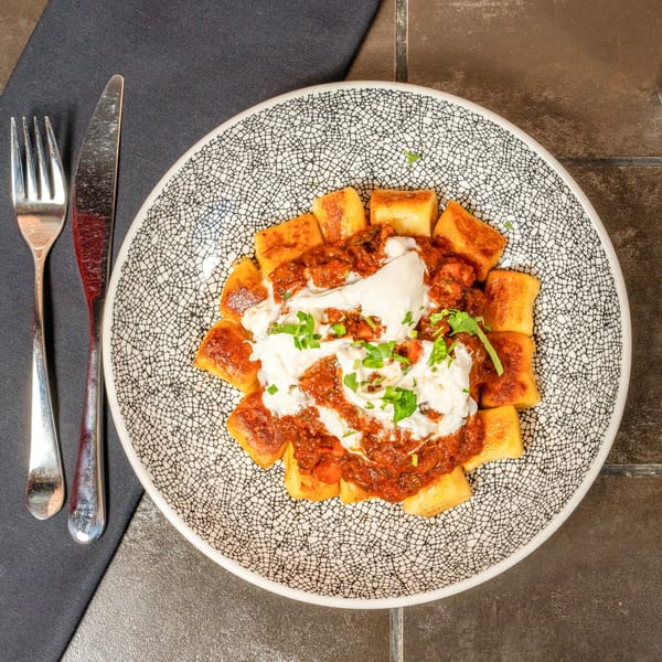 Lena's gnocchi with red sauce, burrata, and fresh herbs on a patterned plate with cutlery.