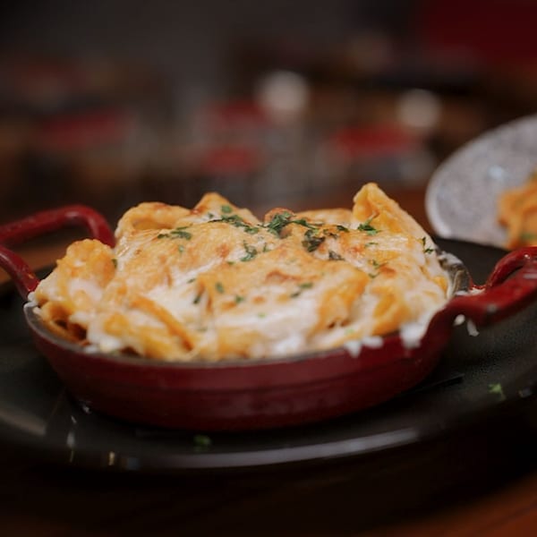 Baked penne pasta with melted cheese and herbs in a red cast iron dish.