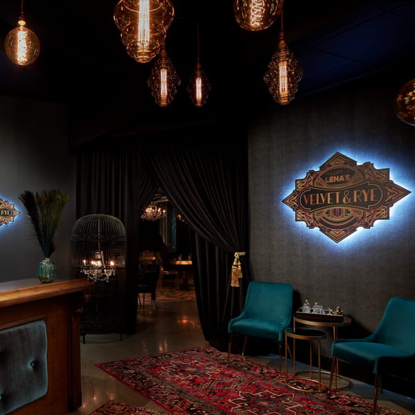 Dark, luxurious waiting area with teal chairs, a red rug, and a glowing "Velvet & Rye" sign.