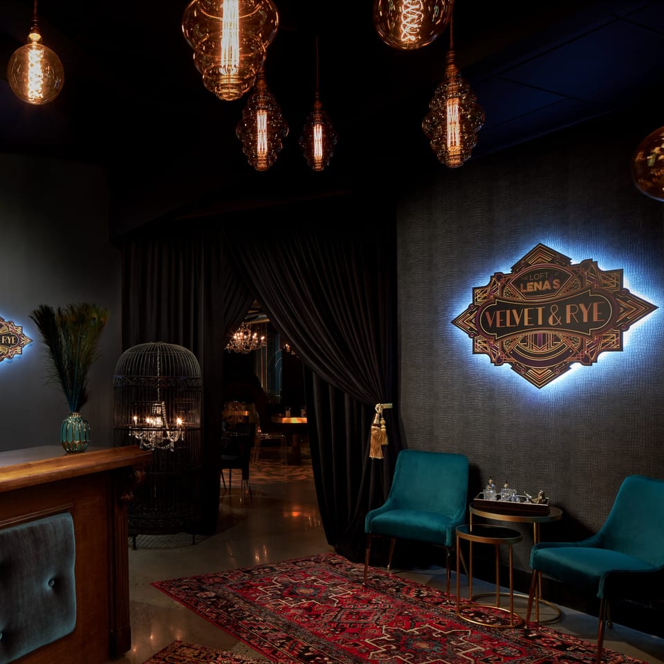 Dark, luxurious waiting area with teal chairs, a red rug, and a glowing "Velvet & Rye" sign.