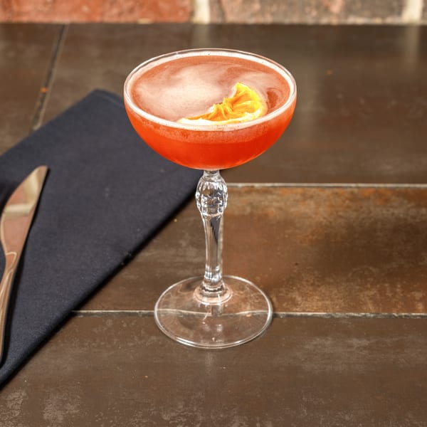 A vibrant red cocktail with a citrus garnish in a coupe glass on a dark table.