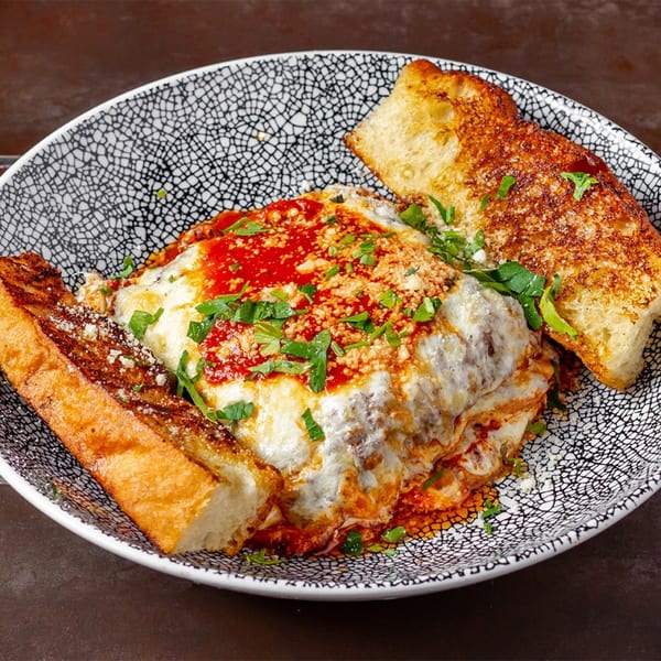 Lena's Wood-Fired Pizza & Tap's baked lasagna with melted cheese, red sauce, and two pieces of garlic bread.