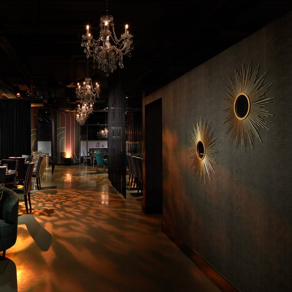 Elegant dining room at Lena's Wood-Fired Pizza & Tap with chandeliers, patterned walls, and warm lighting.