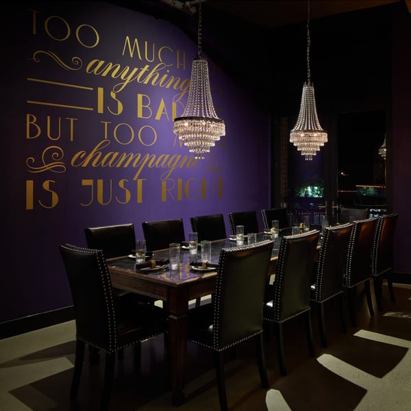 Elegant private dining room with a long table, black chairs, chandeliers, and a purple wall with gold lettering.