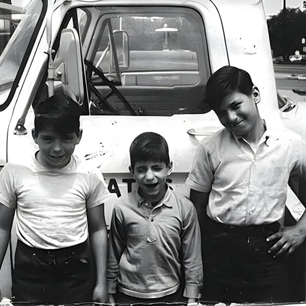 Three young boys stand smiling in front of a white truck, captured in a black and white photo.