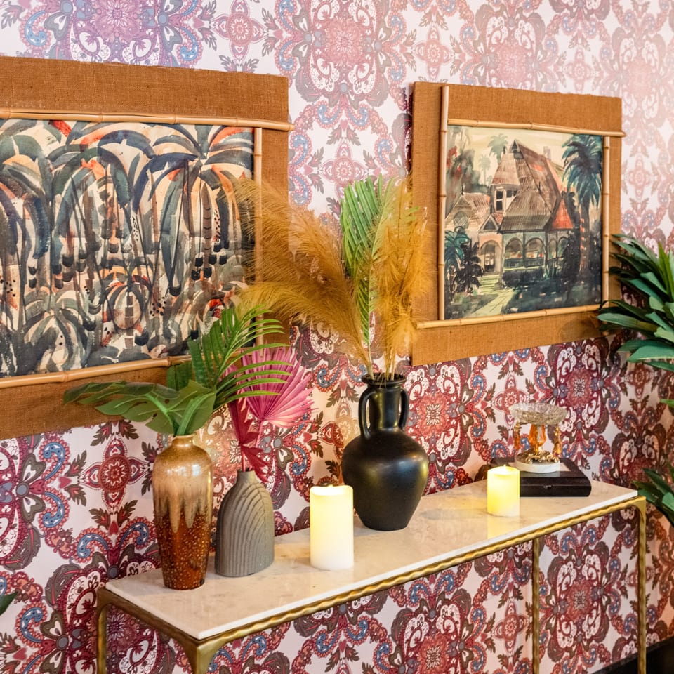 A decorative console table with vases, candles, and framed artwork against patterned wallpaper.