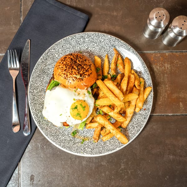 A burger with a fried egg and a side of french fries on a patterned plate.
