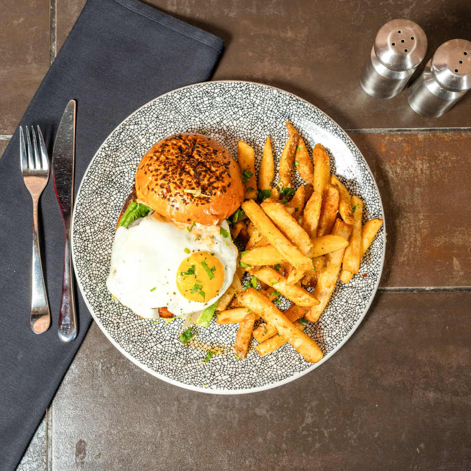 A burger with a fried egg and a side of french fries on a patterned plate.
