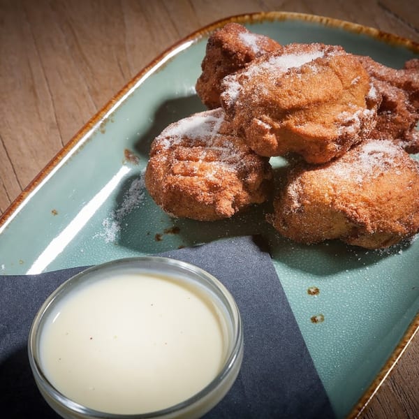 Sugar-dusted Italian zeppole on a teal plate with a side of vanilla dipping sauce.
