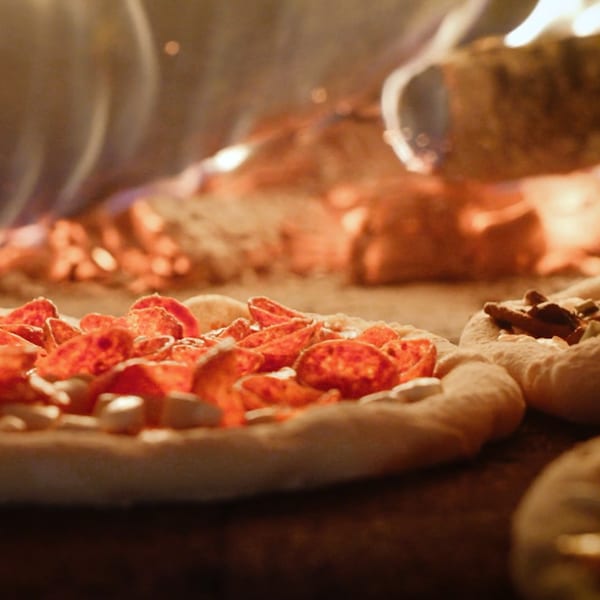 Pepperoni pizza and other small pizzas cooking inside a fiery wood-fired oven at Lena's.