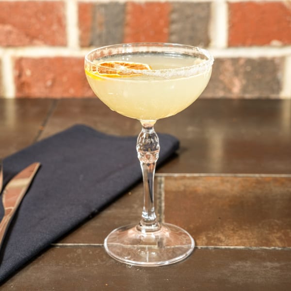 A Lena's Wood-Fired Pizza & Tap cocktail, garnished with a dried orange slice and sugar rim.