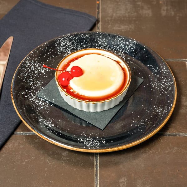 Lena's Panna Cotta dessert with caramel sauce and two bright red cherries on a dark plate.