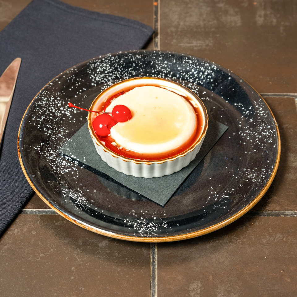 Lena's Panna Cotta dessert with caramel sauce and two bright red cherries on a dark plate.