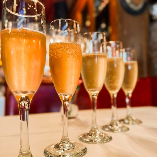 Five flutes of sparkling orange and yellow beverages with bubbles on a white tablecloth.