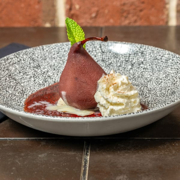 Poached pear dessert with whipped cream, cinnamon, and a mint leaf in a patterned bowl.