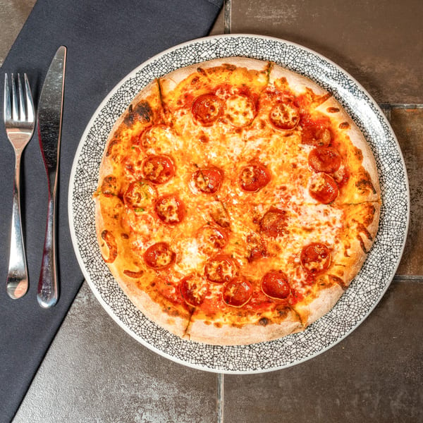 Lena's Wood-Fired Pizza & Tap pepperoni pizza on a patterned plate with cutlery on a dark napkin.