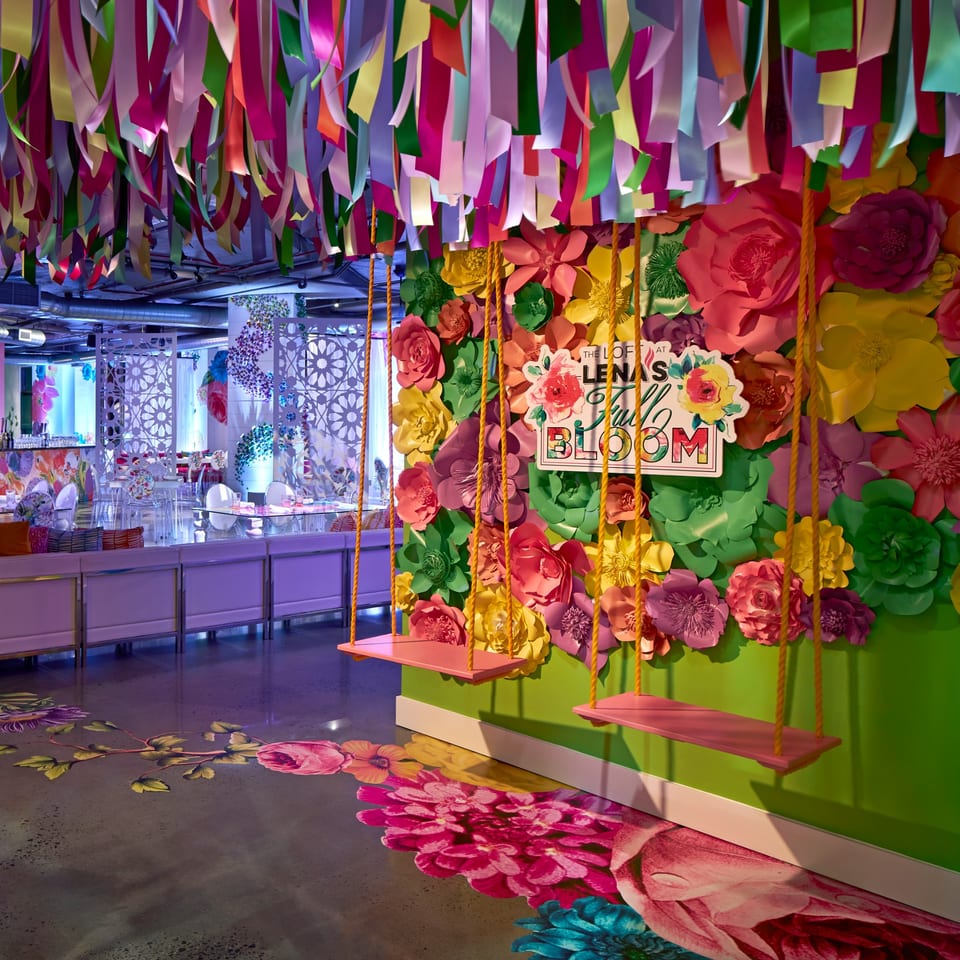 Colorful paper flowers and ribbons adorn a vibrant event space with swings and patterned screens.