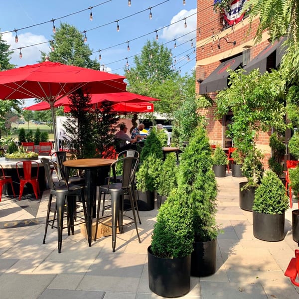 Lena's Wood-Fired Pizza & Tap's outdoor patio with red umbrellas, string lights, and potted plants.