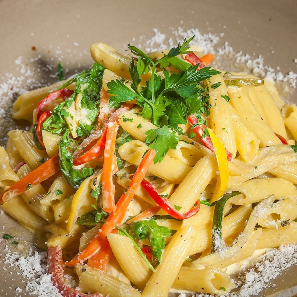 Penne pasta with colorful bell peppers, zucchini, and fresh parsley, sprinkled with Parmesan cheese.