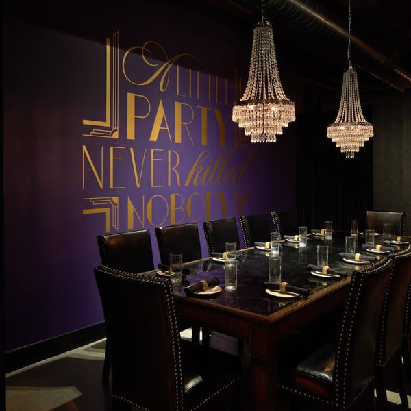 Private dining room with a long dark table, leather chairs, chandeliers, and a purple wall with gold text.