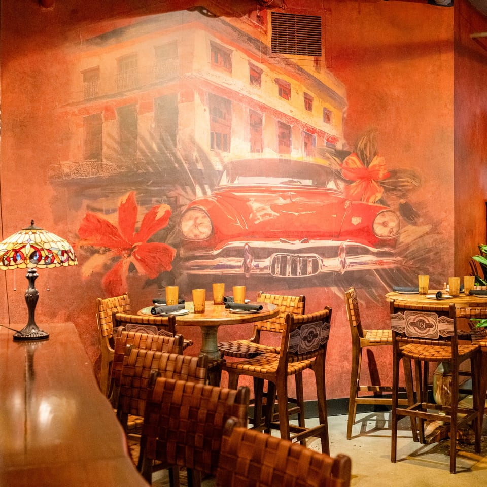 Restaurant interior with a large mural of a red vintage car and building, with tables and chairs.