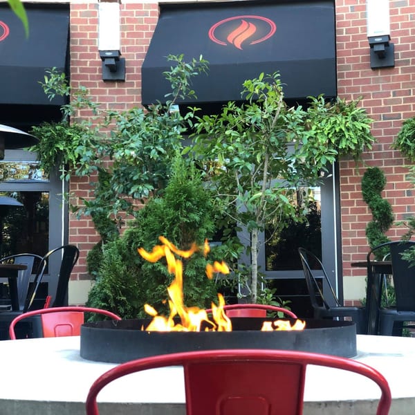 Outdoor patio seating at Lena's Wood-Fired Pizza with a fire pit table and red chairs.