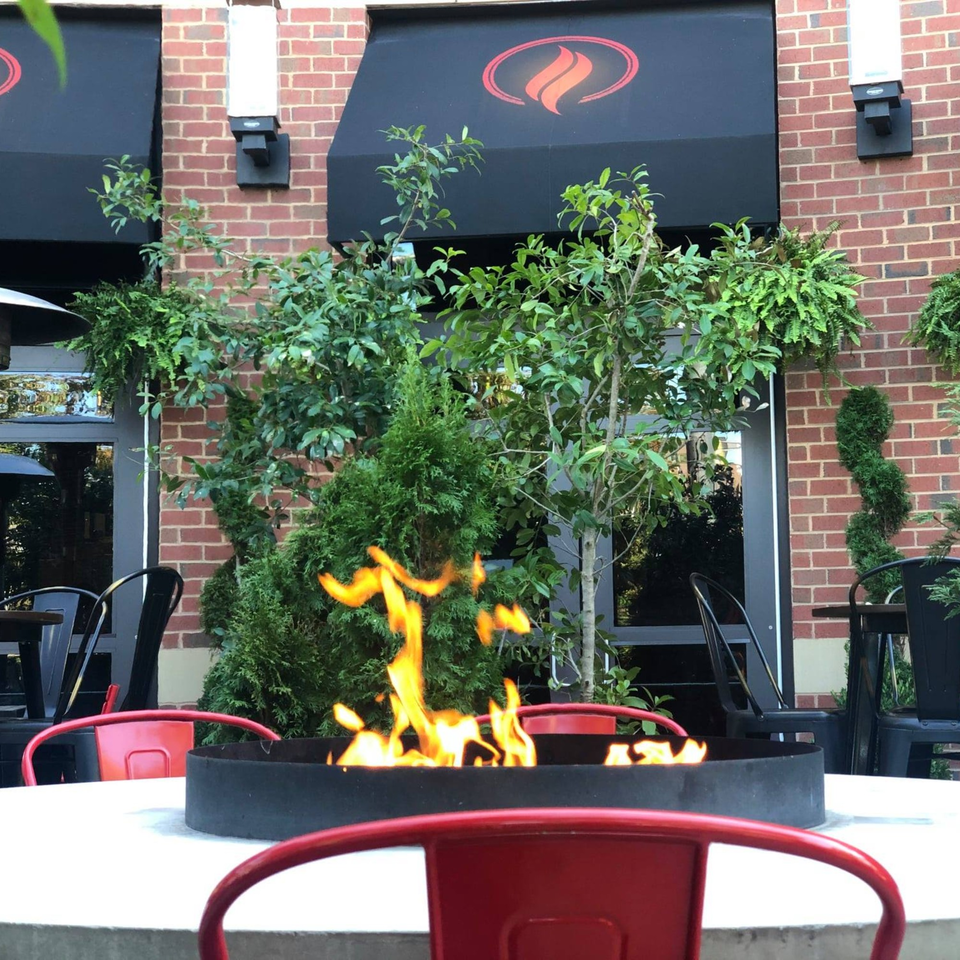 Outdoor patio seating at Lena's Wood-Fired Pizza with a fire pit table and red chairs.