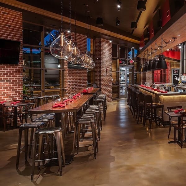 Lena's Wood-Fired Pizza & Tap interior with long communal tables, bar seating, and brick walls.