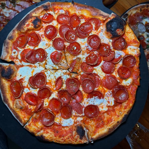 A wood-fired pepperoni pizza from Lena's, with a slice removed, on a dark serving board.