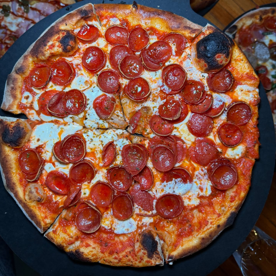 A wood-fired pepperoni pizza from Lena's, with a slice removed, on a dark serving board.