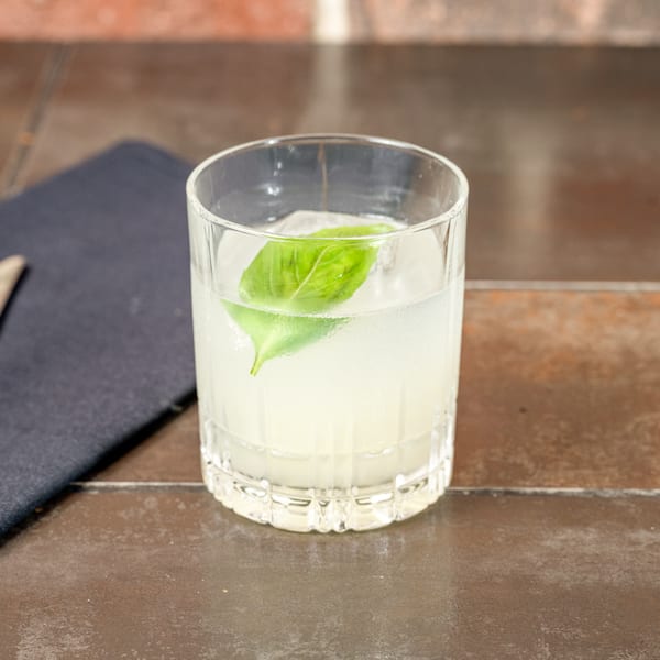 A refreshing Lena's Wood-Fired Pizza & Tap cocktail with basil and ice on a rustic table.