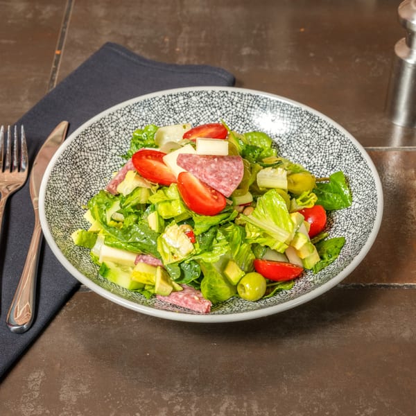 Lena's Italian salad with salami, cheese, tomatoes, olives, and greens in a patterned bowl.